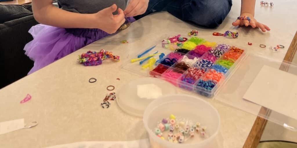 two young children at counter making bracelets with rubber band kit