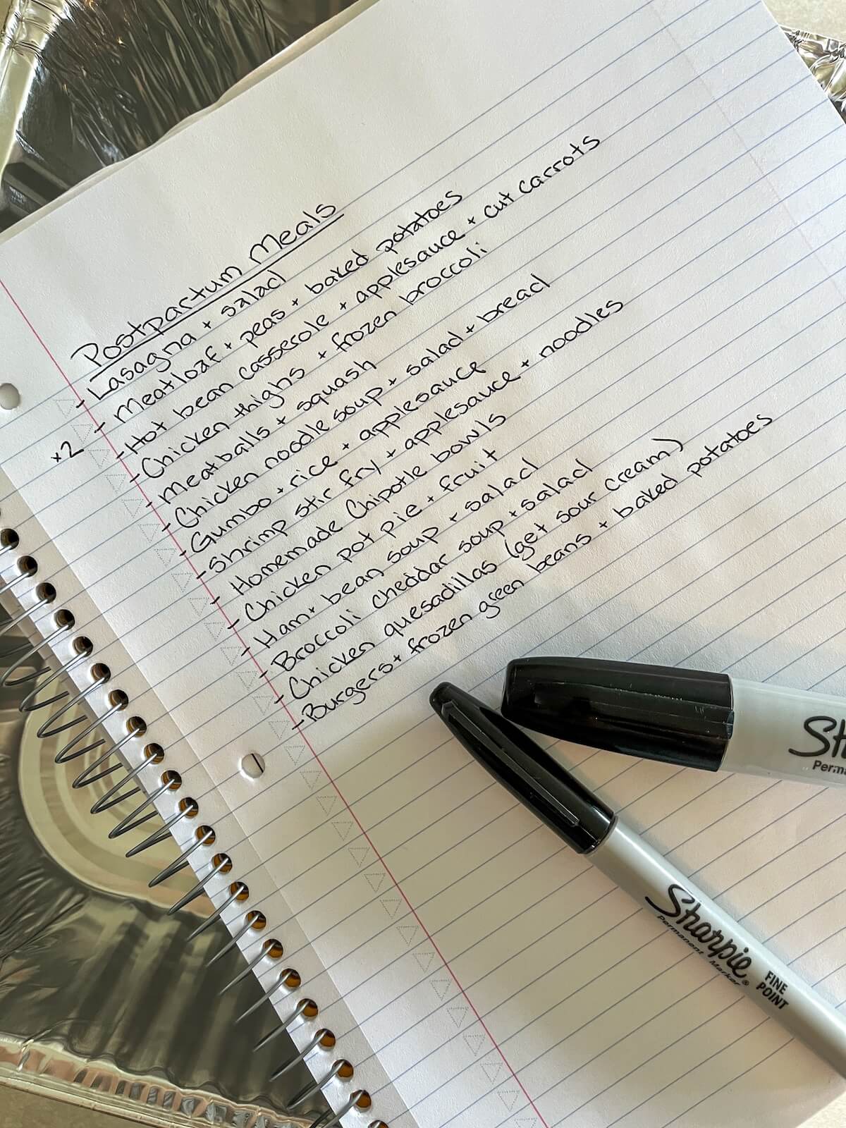 notebook with list of postpartum freezer meals and black sharpies sitting on top