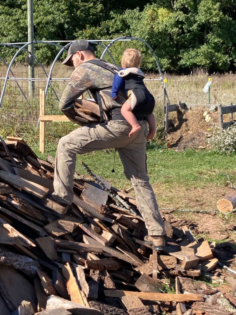 dad with baby on back in ergo while stacking wood
