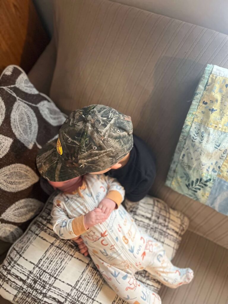 little boy with camo hat holding baby on couch