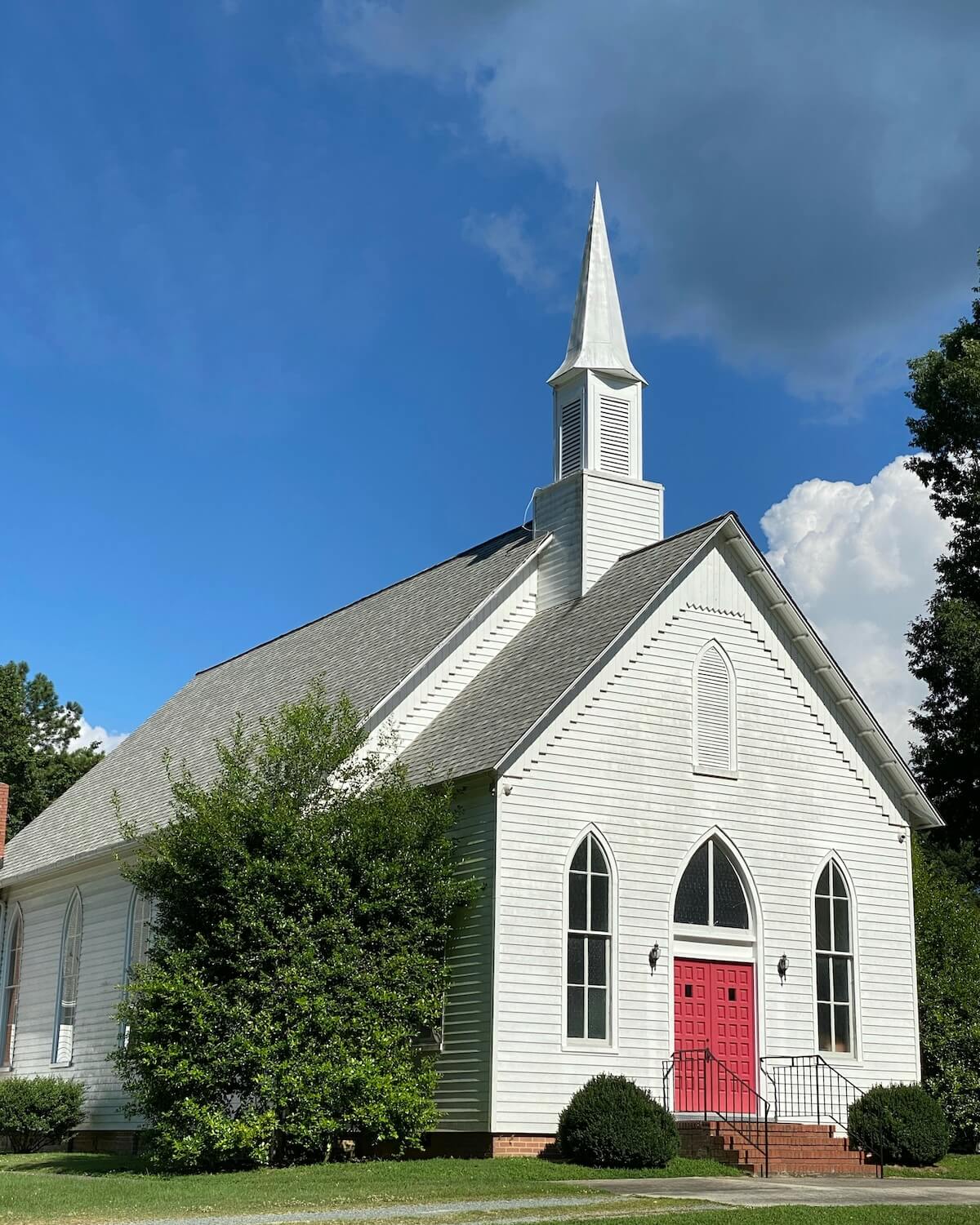 white church in the country with steeple and red door in front of a blue sky
