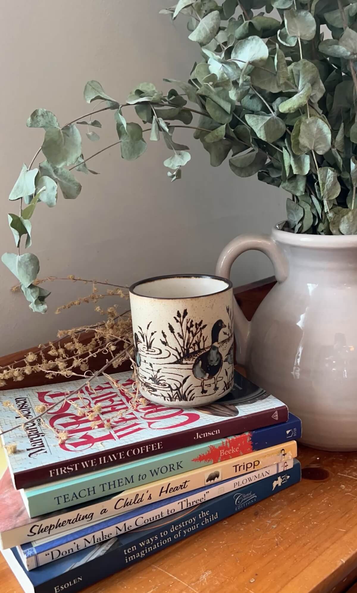 stack of books for christian mothers with a mug of coffee and potted eucalyptus