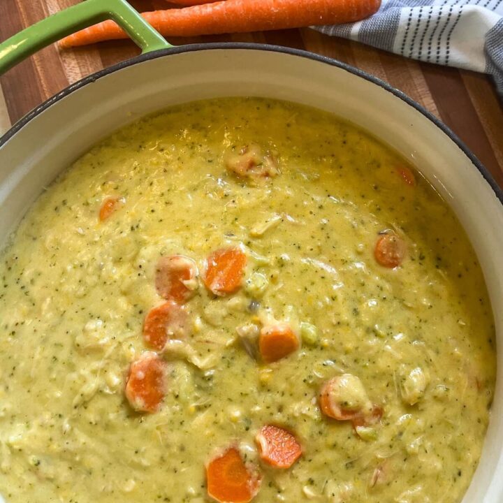 pot of creamy broccoli cheddar chicken soup on wooden cutting board with whole carrots and tea towel