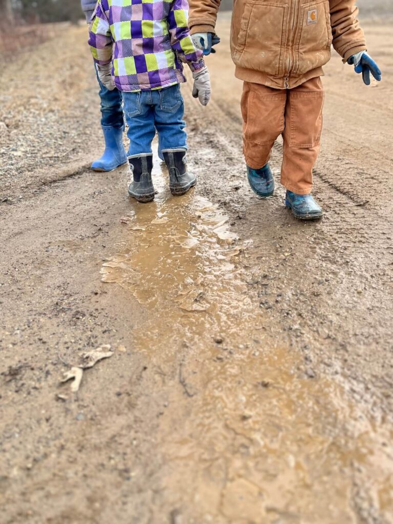 children playing outside in rainboots on muddy road