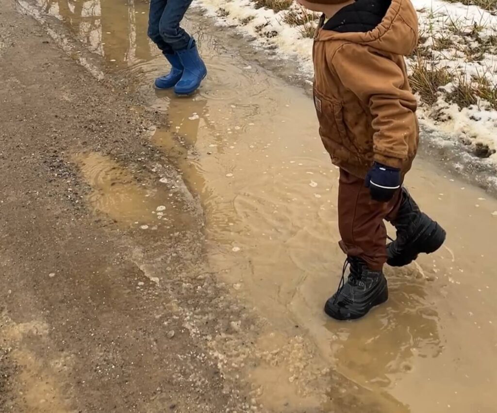 two kids playing in puddles with rain boots