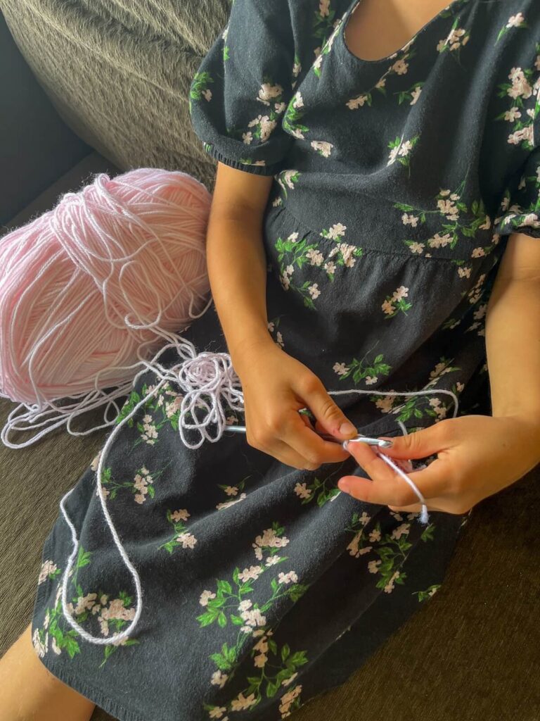 young girl in dress crocheting on couch