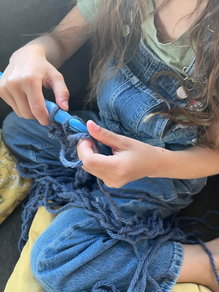 young girl in overalls crocheting